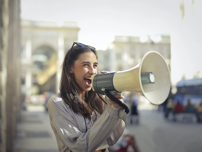 Cheerful young woman screaming into Megaphone